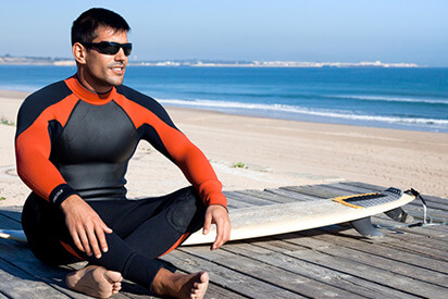 Surfer sitzt mit
                Surfboard und Wassersportbrille am Strand